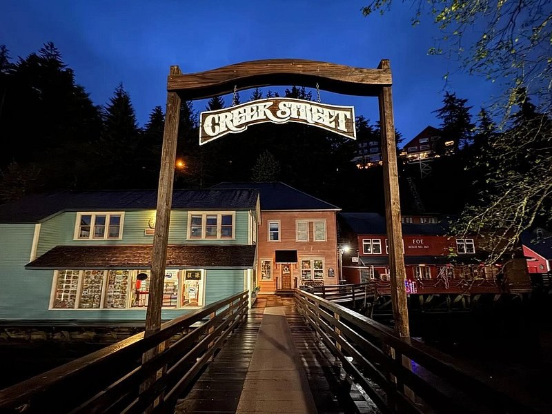 The Creek Street sign over the footbridge at dusk, the boardwalk shops lit behind it