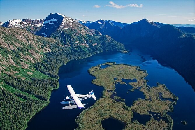 A floatplane over a Misty Fjords inlet and its low green islands, snow on the peaks