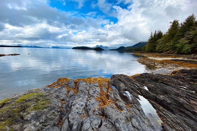 Lichen-covered rocks on a quiet shore, wooded islands across the channel
