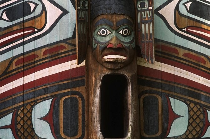 A carved and painted face on a totem pole, framed by formline designs