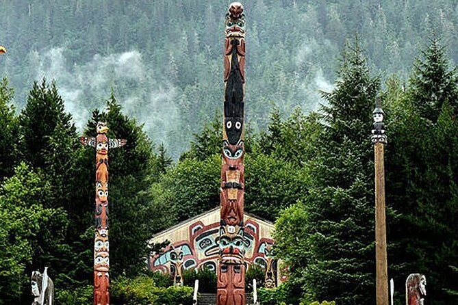 Totem poles and a painted house front rising among tall spruce